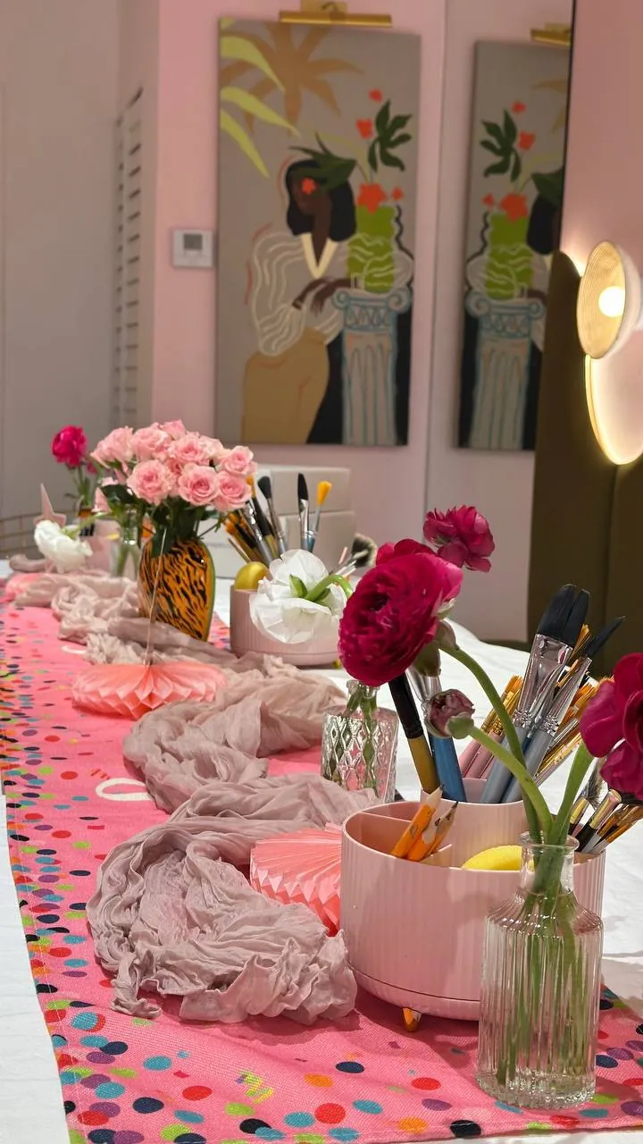 Party table runner with flowers, brushes and a pink paint caddy